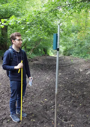 Ein Mann steht neben einem installierten Sensor mit einem Zollstock in der Hand