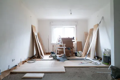Unfertiger Raum mit weißen Wänden, Fenstern, Bauholz, Werkzeugen und Baumaterialien auf dem Boden