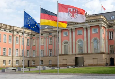 Zu sehen ist der Landtag in Potsdam vor dem drei Fahnen wehen: EU, Deutschland, Brandenburg