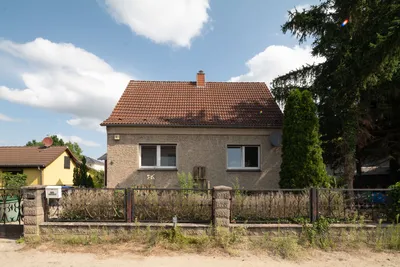 Einfamilienhaus mit rotem Ziegeldach, zwei Fenstern und kleinem Garten hinter einem niedrigen Zaun