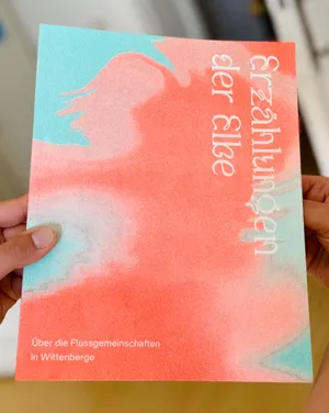 Hand legt sich auf ein Buch mit abstrakter, pastellfarbener Covergestaltung und dem Titel 'Erzählungen der Elbe'