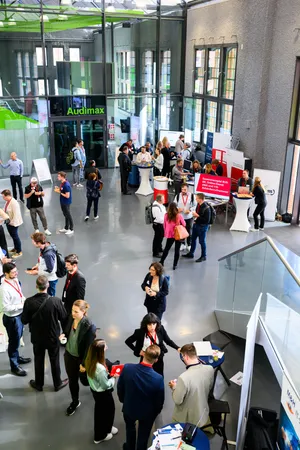 Vogelperspektive auf das lichtdurchflutete Atrium des Audimax der TH Wildau. Zahlreiche Besucherinnen und Besucher schlendern über den Markt der Möglichkeiten und informieren sich an den Ständen digitaler Landesprojekte.