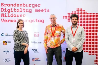 Mitwirkende des Teams Digitalisierung stehen lächelnd vor der offiziellen Fotowand der Veranstaltung mit der Aufschrift „Brandenburger Digitaltag meets Wildauer Verwaltungstag“.