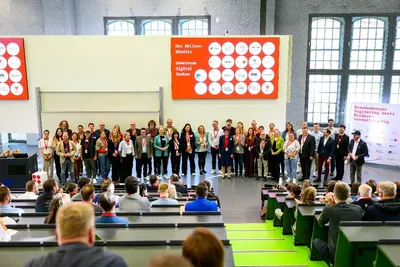 Großes Abschluss-Gruppenfoto vor der Hauptbühne. Zahlreiche Mitwirkende, Partner des Aktionsbündnisses und Teilnehmende stehen gemeinsam vor der Projektionsfläche mit dem Logo „Das Aktionsbündnis – Gemeinsam Digital Denken“.