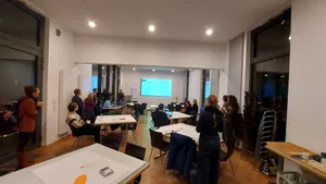 Eine Gruppe von Menschen, stehend und sitzend, in einem großen Seminarraum. 
