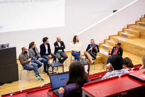 Menschen in einer Podiumsdiskussion auf Stühlen in einem Hörsaal
