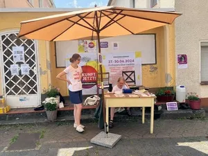 Eine Person unter einem Sonnenschirm vor einem Stand