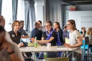 Zu sehen sind Menschen, die zusammen an einem Tisch stizen 