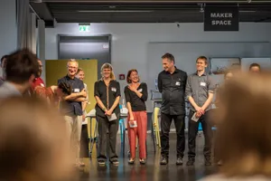 Zu sehen sind Menschen, die nebeneinander im Kreis stehen