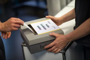 Zu sehen ist eine Briefbox und eine Hand, die einen Brief dort hineinwirft