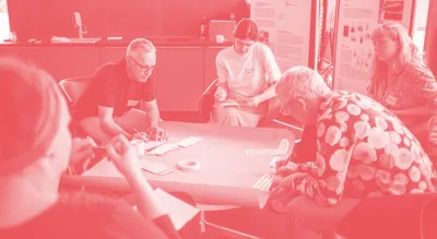 Gruppe von fünf Personen sitzt um einen Tisch und arbeitet gemeinsam an Unterlagen