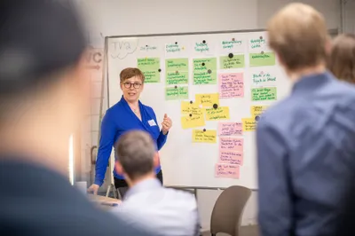 Eine Frau präsentiert ein Flipchart mit geschriebenen Karten vor einer Gruppe.