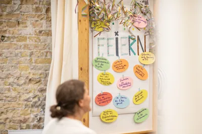 Zu sehen ist eine Frau vor einem Flipchart mit Girlanden, an dem persönliche Erfolge gesammelt werden.