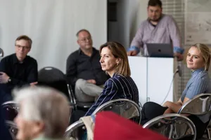 Eine Gruppe von Personen sitzt in Stühlen in einem Raum und führt ein Gespräch.  