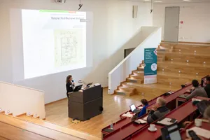 Eine Frau hält eine Präsentation vor einem Publikum im Vorlesungssaal. 