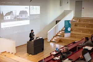 Eine Frau hält eine Präsentation vor einem Publikum im Vorlesungssaal.  