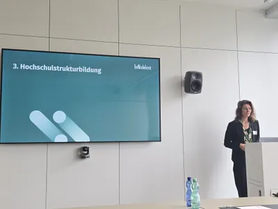 Eine Frau steht vor einem großen Screen und hält einen Vortrag.