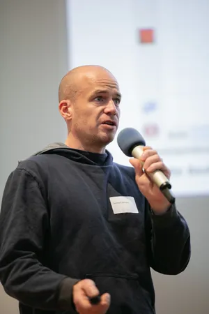 Ein Mann spricht in ein Mikrofon, im Hintergrund sind die Präsentationsfolien zu sehen