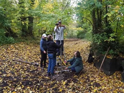 Zu sehen sind mehrere Menschen in einem mit Laub bedeckten Fußbett, die einen Sensor installieren.