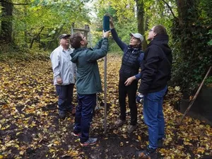 Zu sehen sind mehrere Menschen in einem mit Laub bedeckten Fußbett, die einen Sensor installieren.