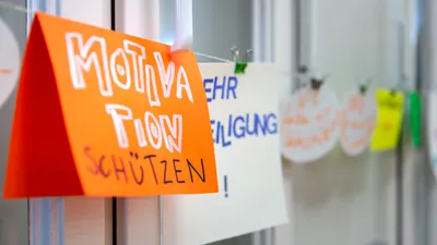 Zu sehen sind bunte Zettel auf denen etwas drauf steht, aufgehängt an einer Schnur