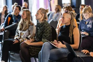 In mehreren Stuhlreihen sitzen Menschen und lauschen einem Vortrag