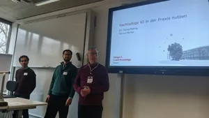 Drei Männer stehen vor einem Bildschirm mit der Präsentation 'Nachhaltige KI in der Praxis nutzen'.