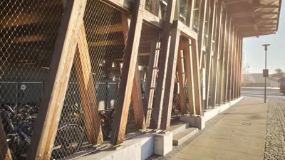 Holzstützen mit Metallgittern an einem Gebäude entlang eines gepflasterten Gehwegs bei Tageslicht.