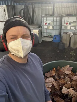 Zu sehen ist Thomas Berg mit Gehör- und Atemschutz vor einem großen Behälter Laub.