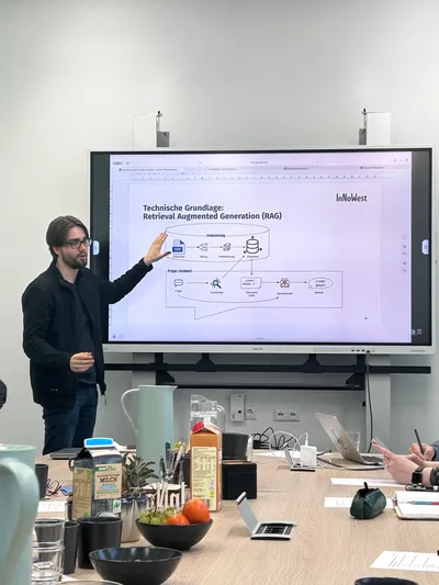 Eine Person erklärt mit erhobener Hand vor einem Whiteboard eine Grafik zur technische Funktion eines RAG KI Chat Bots.