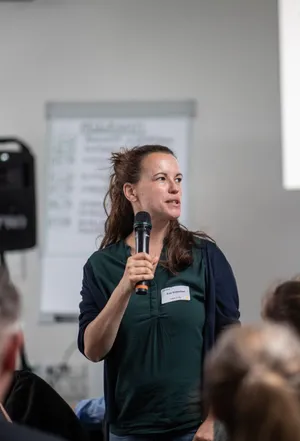 Eva hält eine Präsentation in einem kleine Raum voller Menschen.