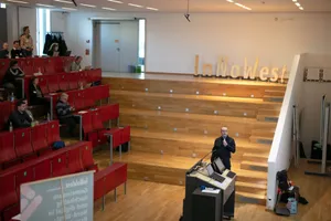 Ein Mann steht in der Mitte eines Hörsaales und spricht in ein Mikrofon