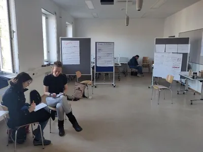 Zwei Personen sitzen vor mehreren Pinnwänden in einem Seminarraum und bereiten einen Workshop vor.